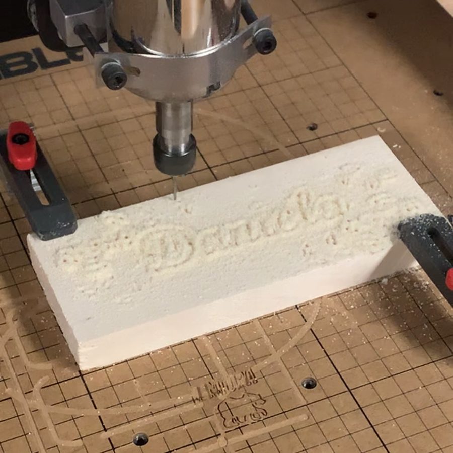 Aspen wood nameplate on the carving machine bed with the name Daniela and leaf designs carved in