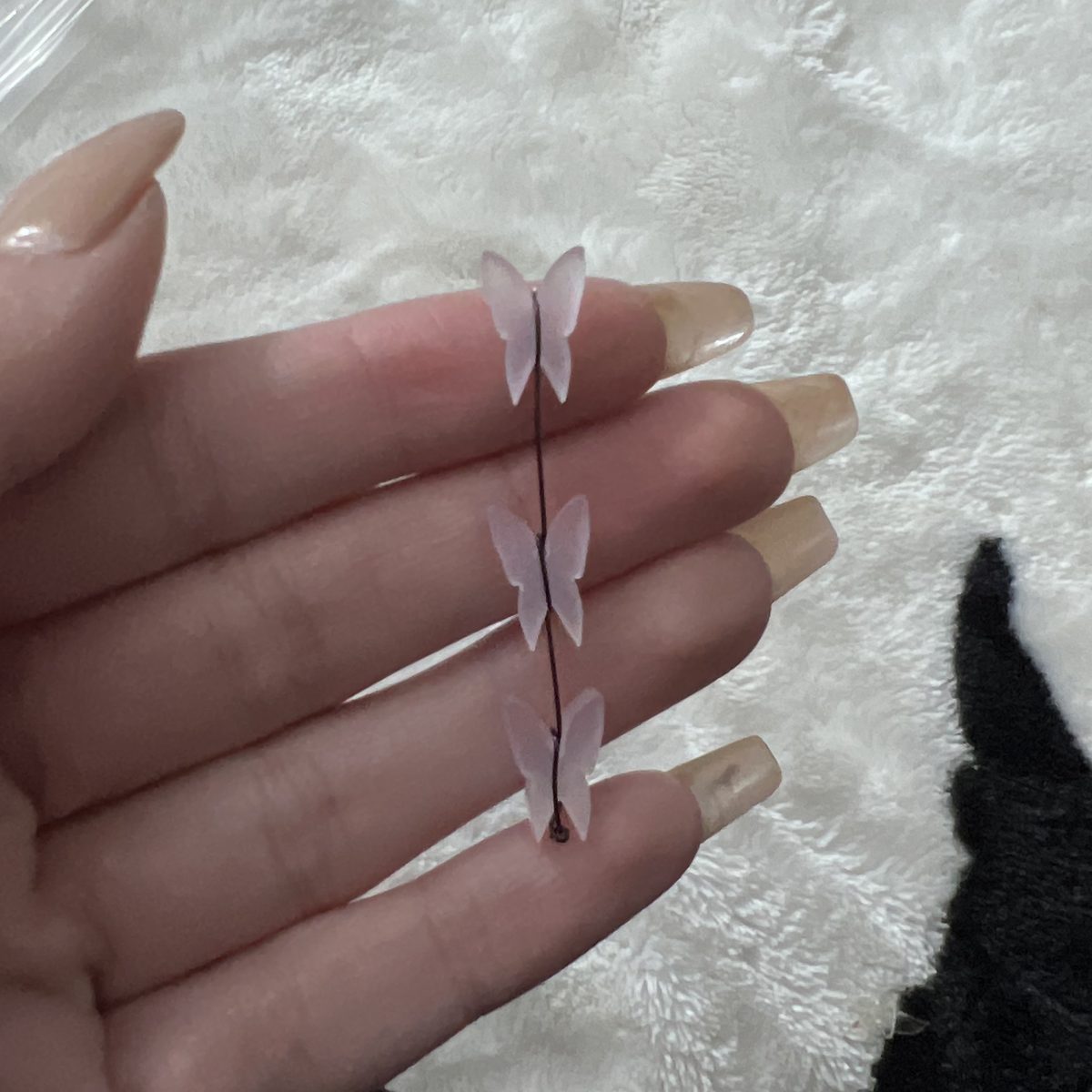 Three small laser-cut pink acrylic butterflies strung on a wire, held in an open hand